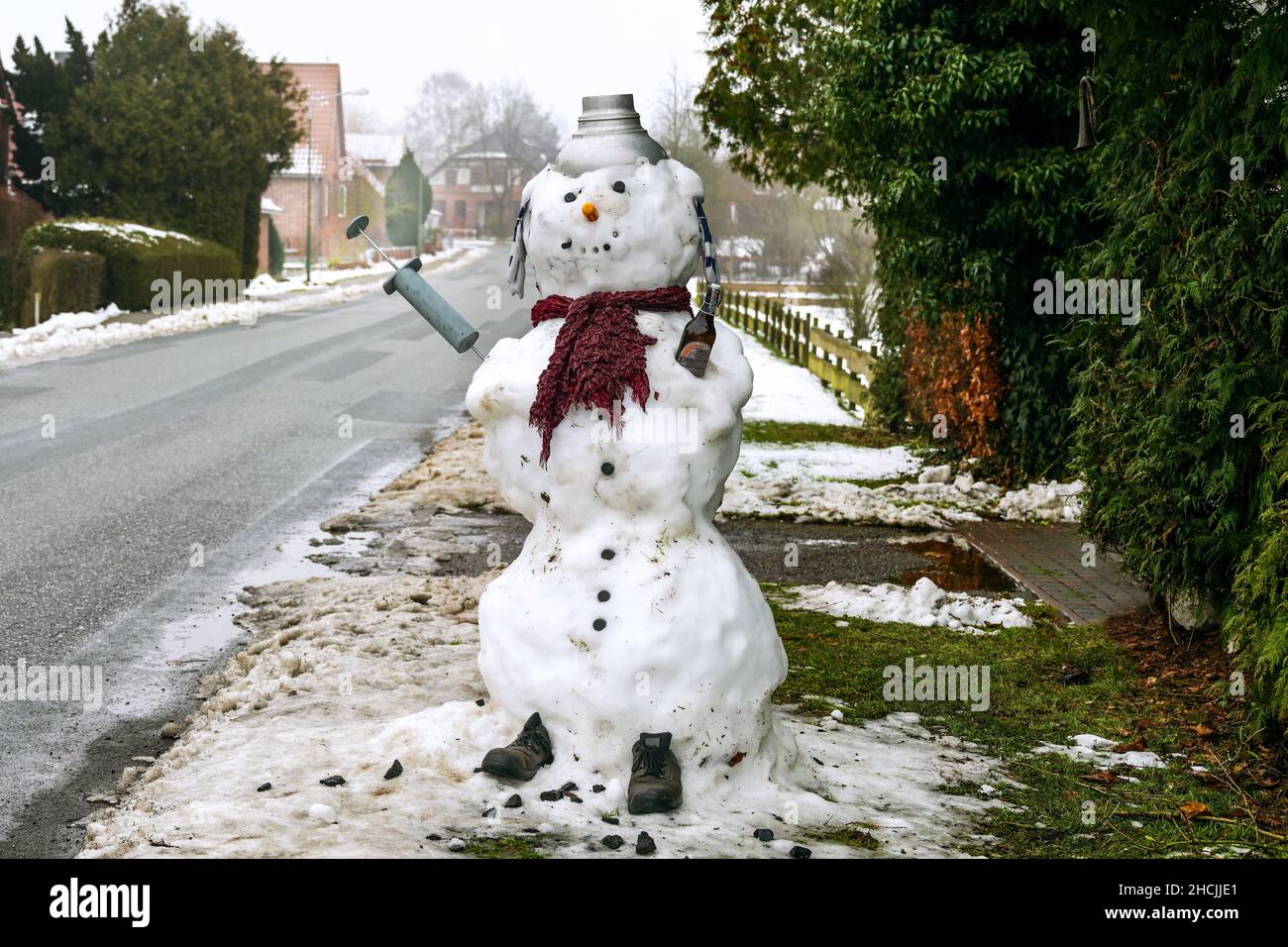 Carlow, Germania, 29 dicembre 2021: Scongelamento di un pupazzo di neve con siringa di vaccinazione contro il covid-19, sciarpa, cappello, scarpe e una bottiglia di birra allestita su un ambiente rurale v Foto Stock