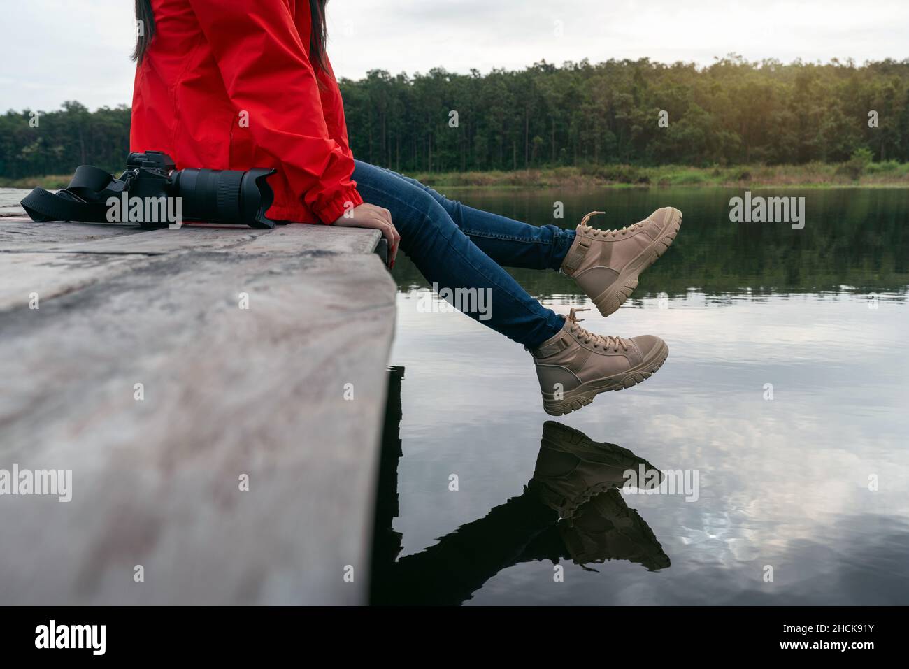 Altalena turistica uno dei piedi vicino alla superficie dell'acqua, Donna si rilassa presso il lago e seduto su un molo di legno. Foto Stock