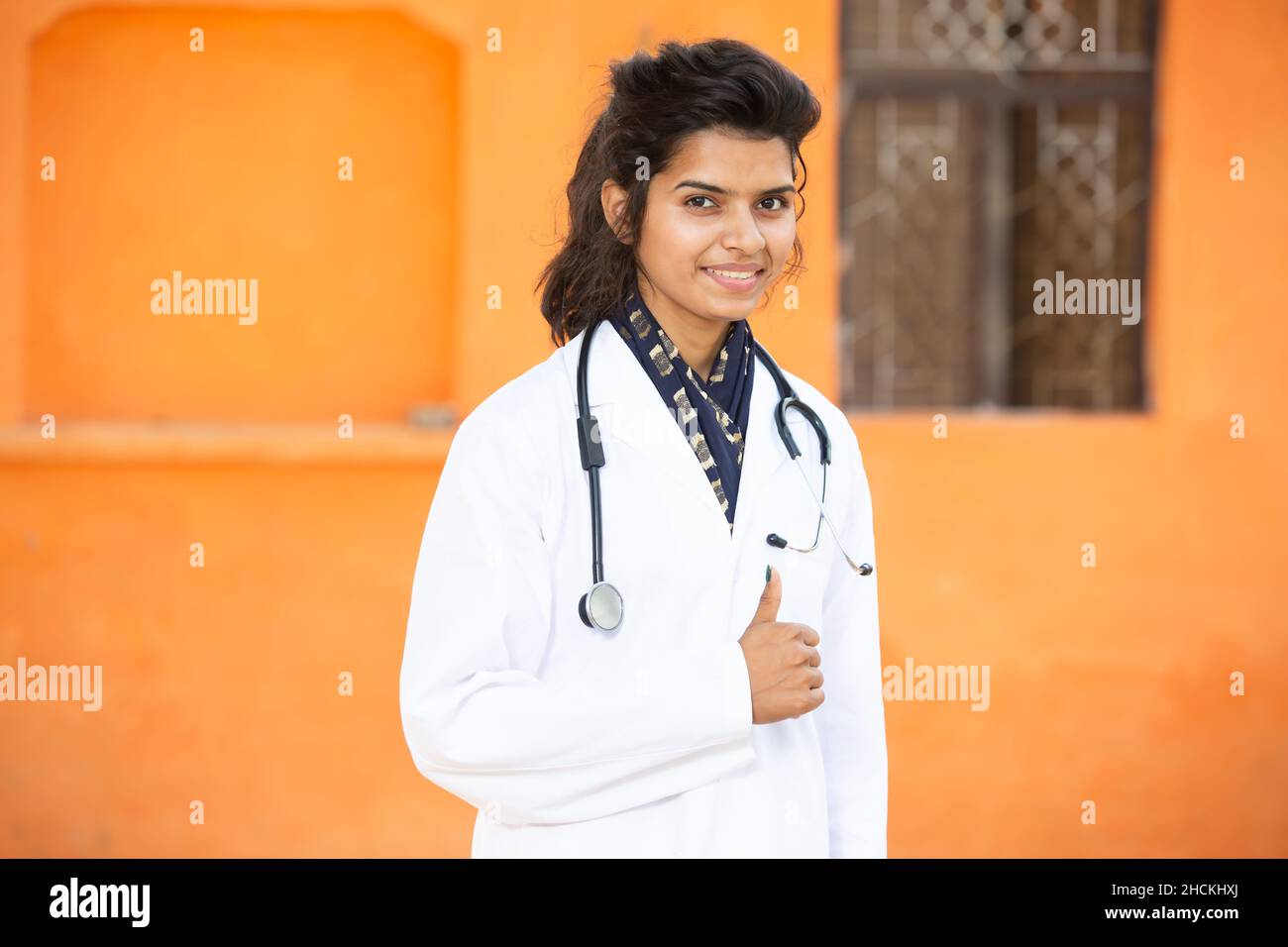 Ritratto di giovane ragazza indiana sorridente medico indossando stetoscopio e grembiule in piedi do thumbs up, sta guardando la fotocamera con emozioni positive ag Foto Stock