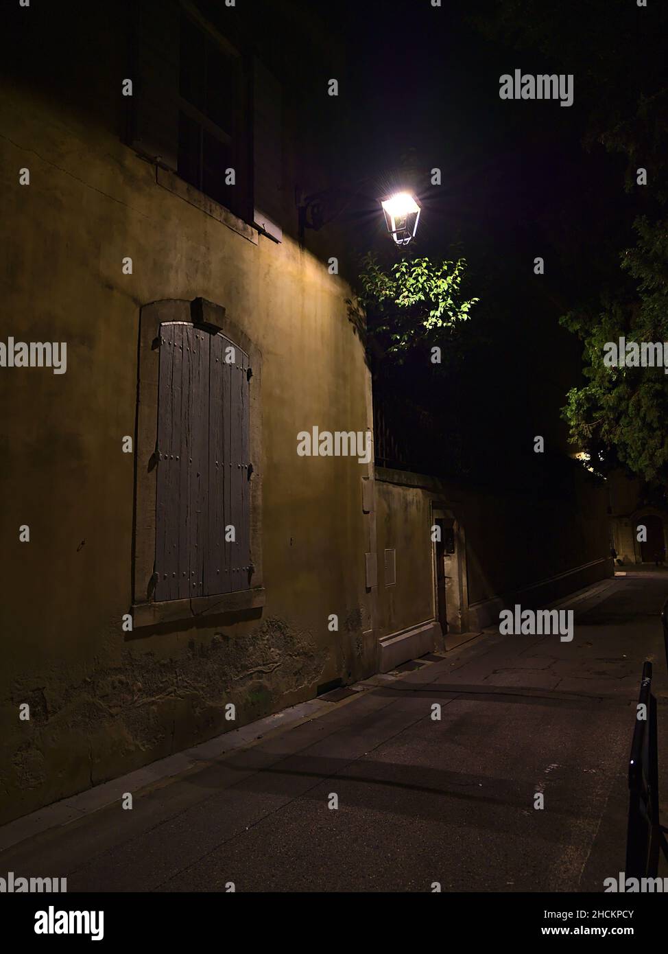 Vicolo stretto con alberi nel centro storico della città Arles nella regione della Provenza, Francia con lampada da strada e finestra chiusa di un edificio tradizionale. Foto Stock
