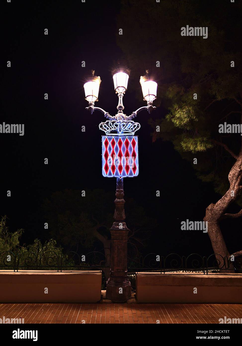 Vista frontale della vecchia luce di strada in ferro di notte nel centro storico di Monaco (Monaco-Ville) sulla Costa Azzurra con lo stemma illuminato. Foto Stock