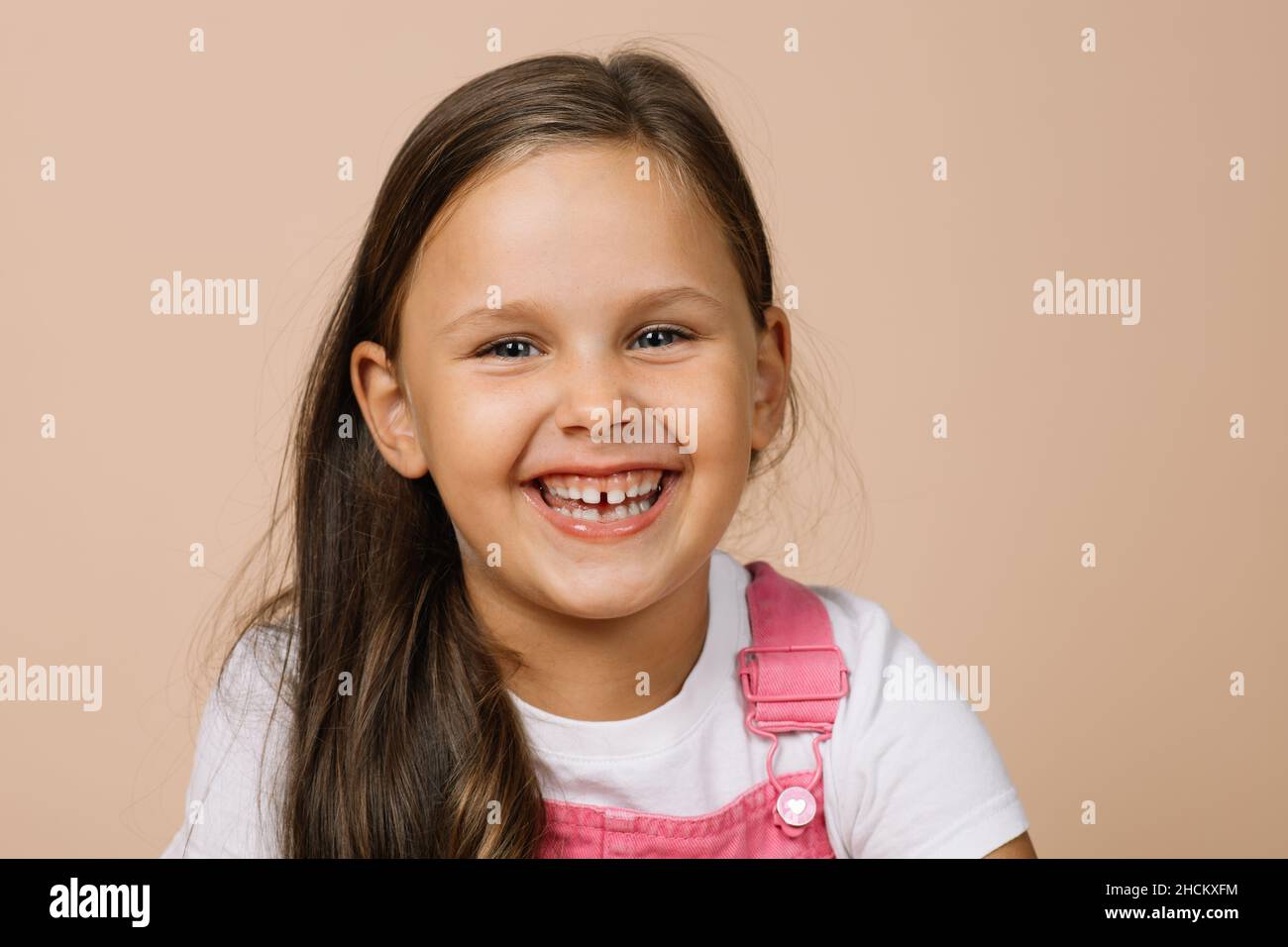Primo piano volto bambino con occhi luminosi e sorriso felice eccitato con i denti guardando la macchina fotografica indossando un tuta rosa brillante e una t-shirt bianca su Foto Stock