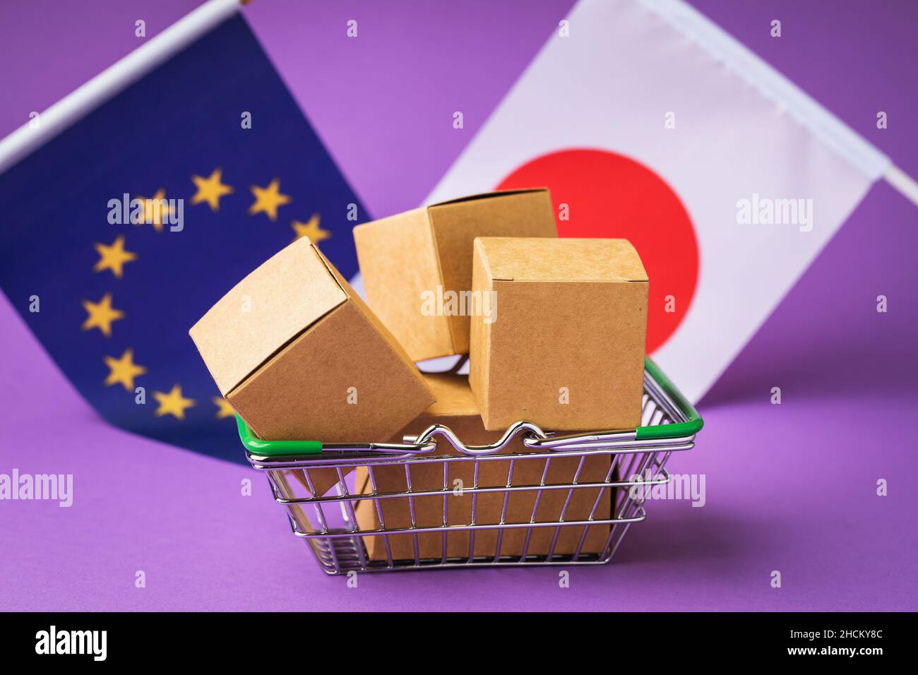 Scatole di cartone in un cestino alimentare, bandiere del Giappone e dell'Unione europea su uno sfondo colorato, il concetto di commercio tra paesi Foto Stock