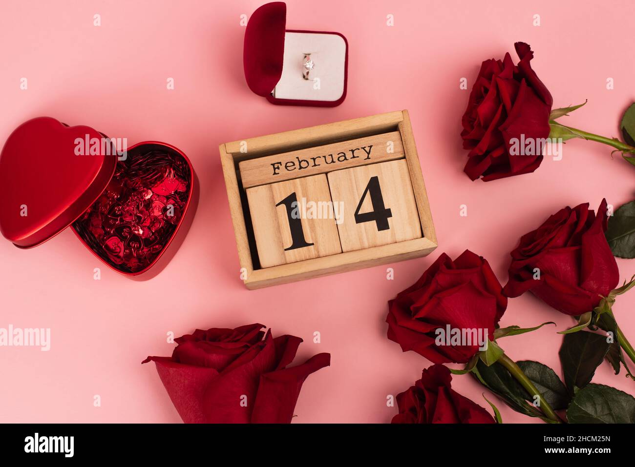 vista dall'alto delle rose rosse vicino al calendario con scritta, confetti e anello di fidanzamento del 14 febbraio su rosa Foto Stock