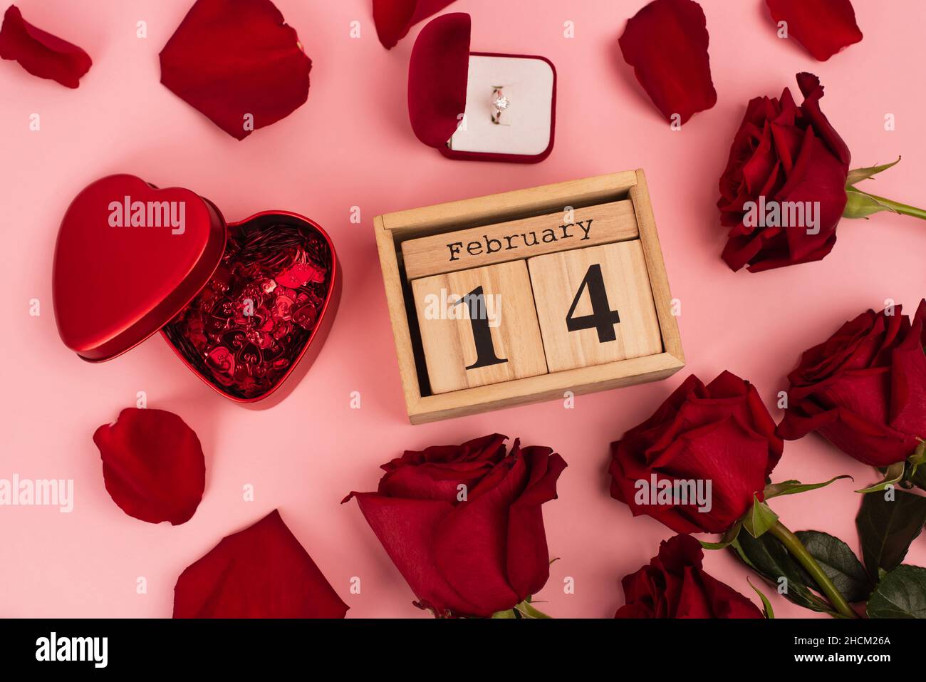 vista dall'alto delle rose rosse vicino al calendario con 14 febbraio, confetti e anello d'aggancio intorno ai petali rosa Foto Stock