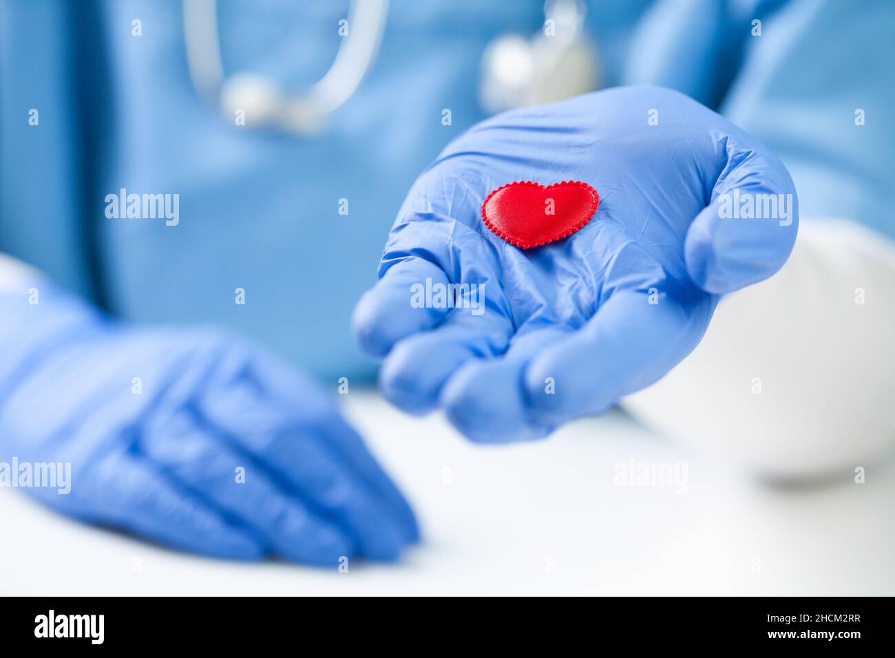 Cardiologo indossare guanti chirurgici protettivi che tengono rosso il cuore di peluche in palmo aperto, concetto di assistenza sanitaria, prevenzione e protezione dei pazienti Foto Stock