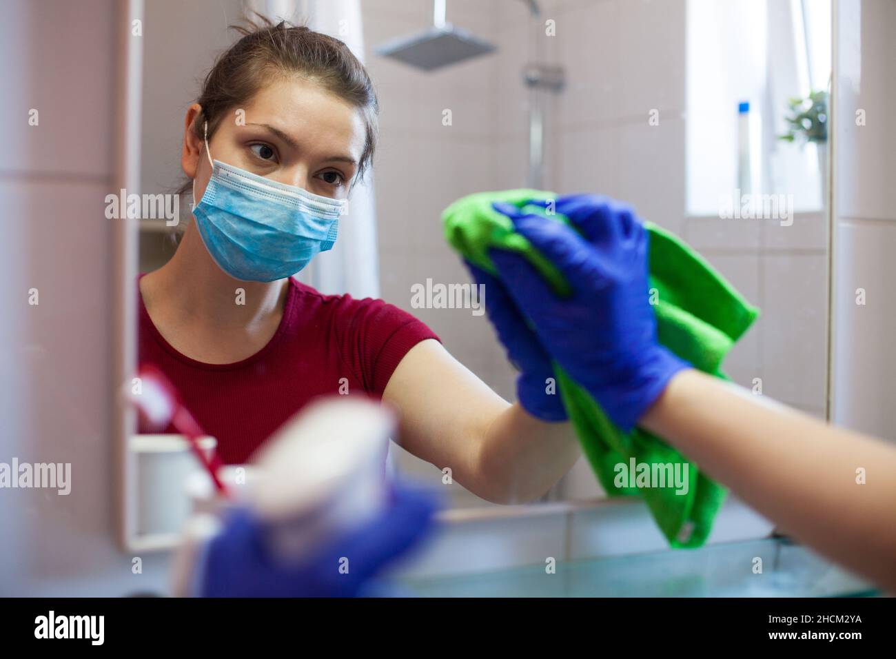 Giovane donna caucasica che indossa maschera facciale e guanti protettivi disinfezione gabinetto con antibatterico spray, aumento delle misure igieniche preventive Foto Stock