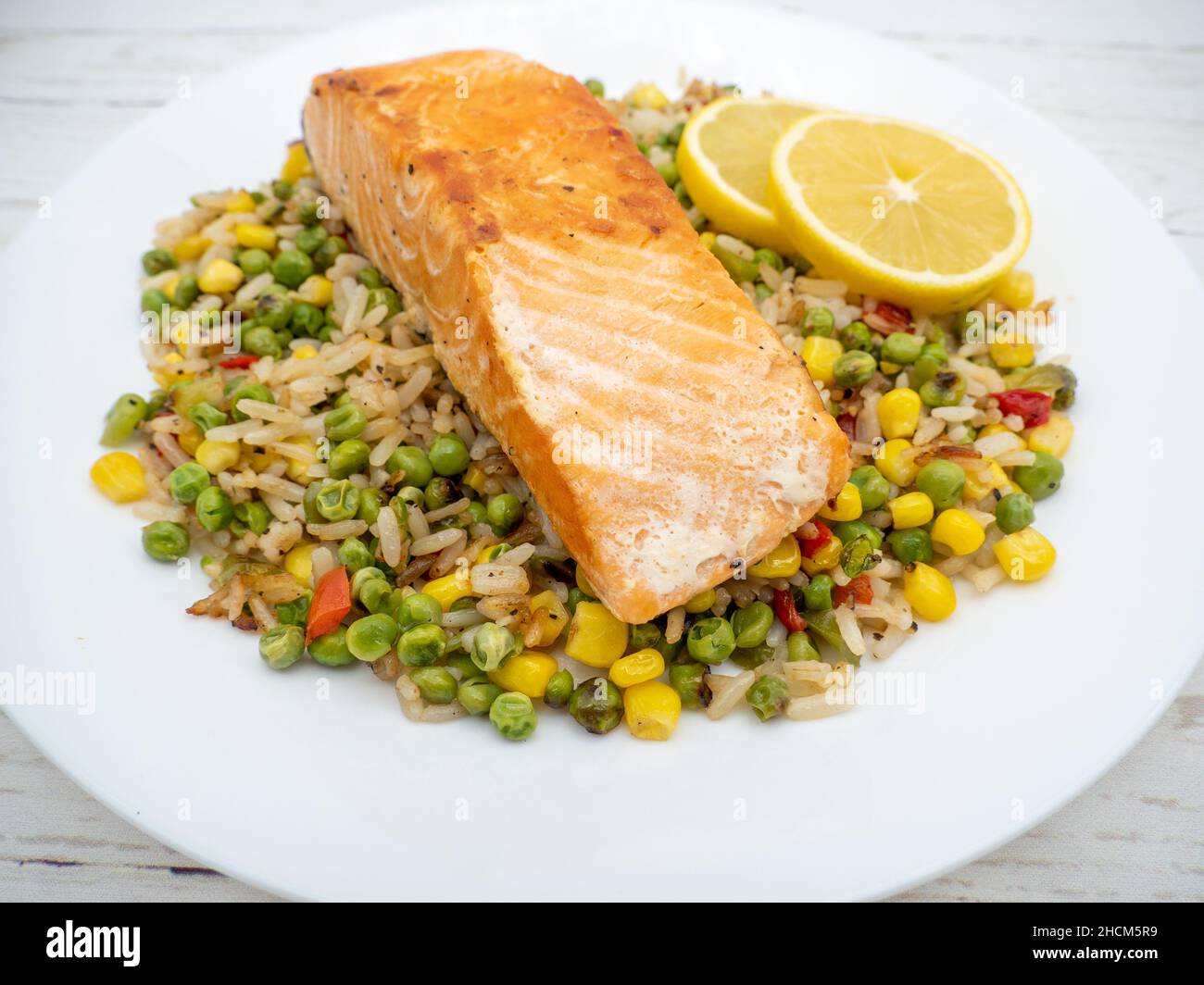 Primo piano di una bistecca di salmone su riso con verdure e due pezzi di limone su un piatto bianco Foto Stock