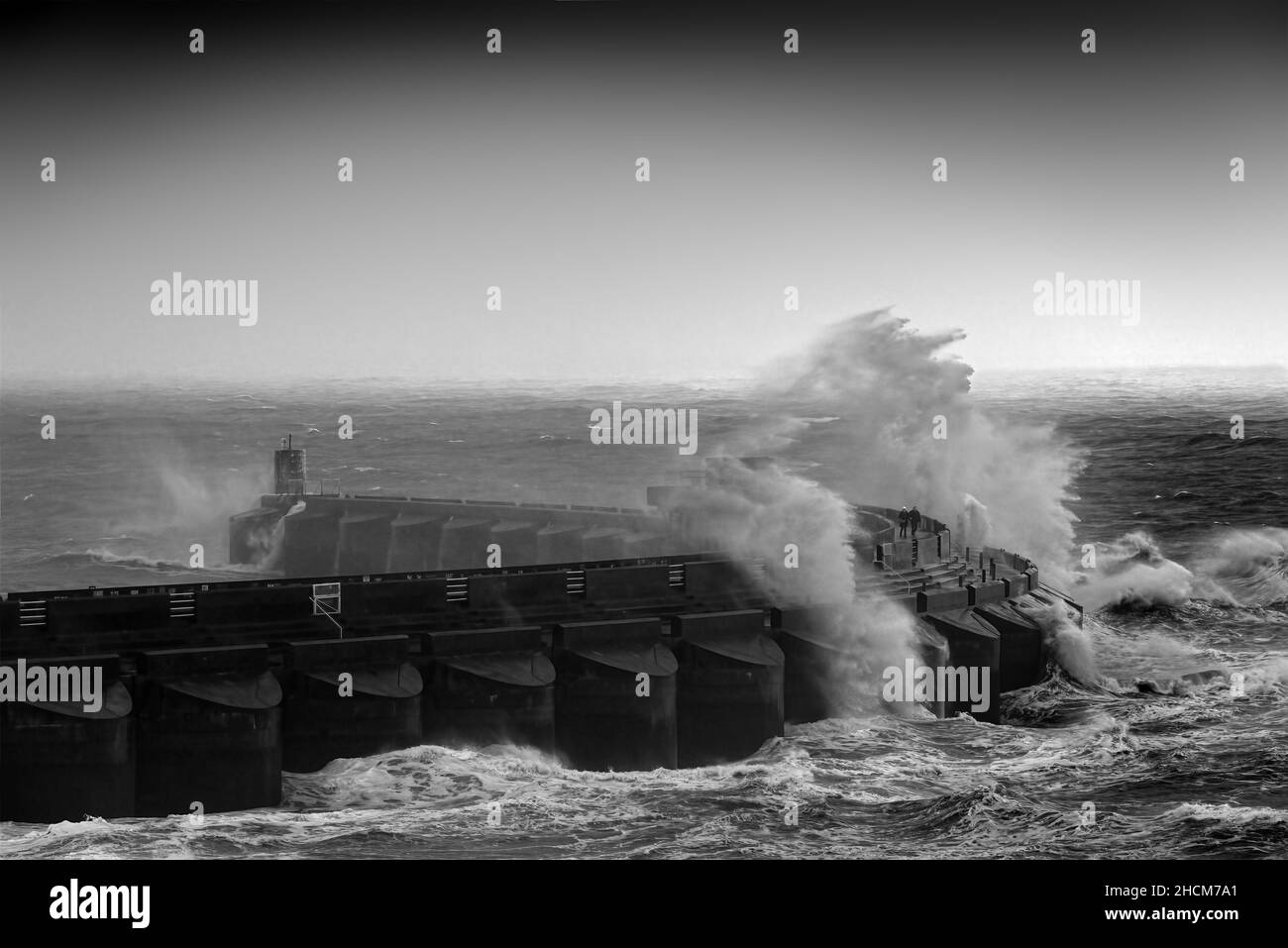 coppia che cammina sul braccio del porto turistico in tempesta con le onde che si infrangono intorno a loro Foto Stock