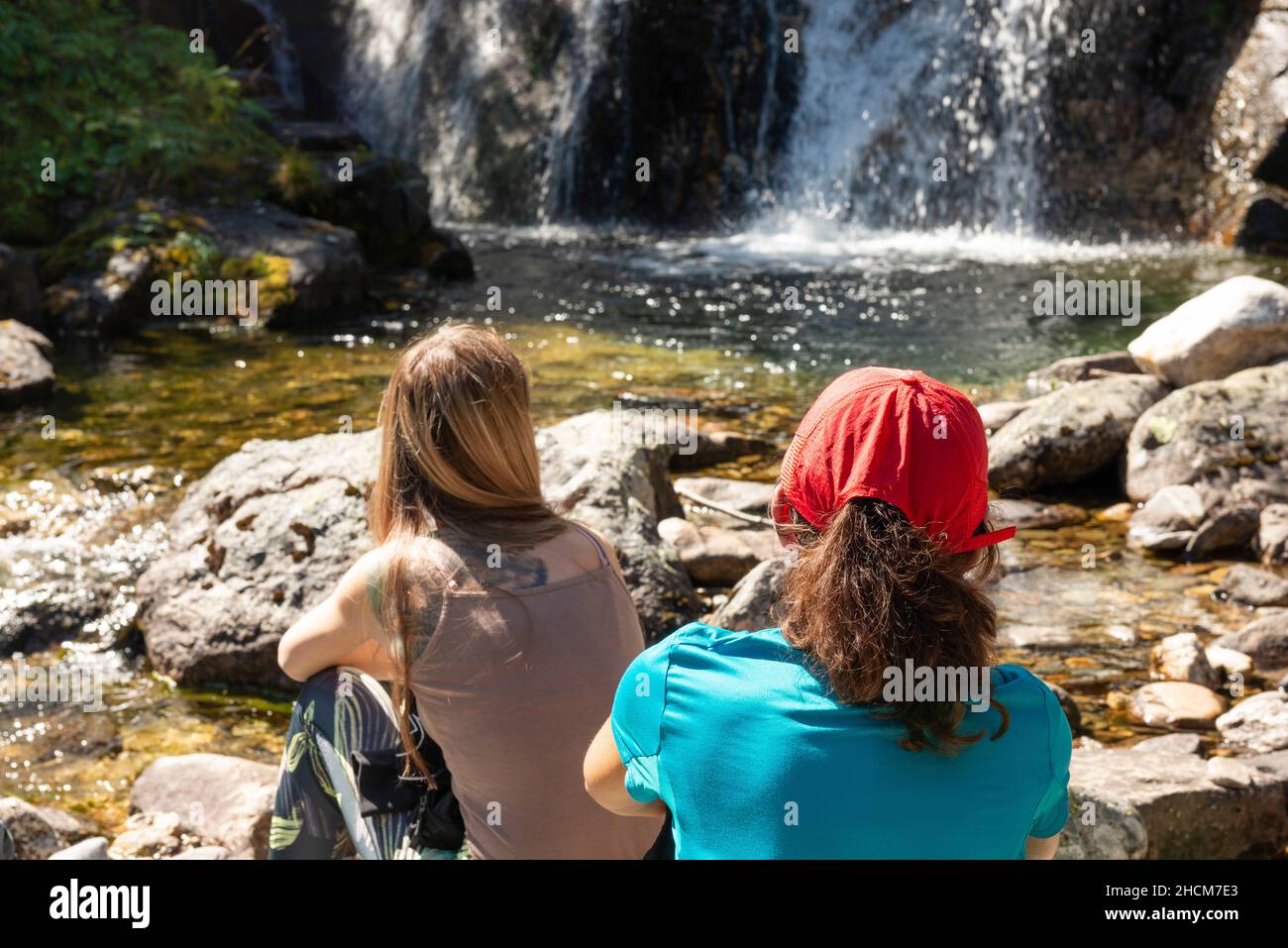 Vista posteriore di due escursionisti donne rilassarsi in una piccola cascata di fiume di montagna a Rila montagna, Bulgaria Foto Stock