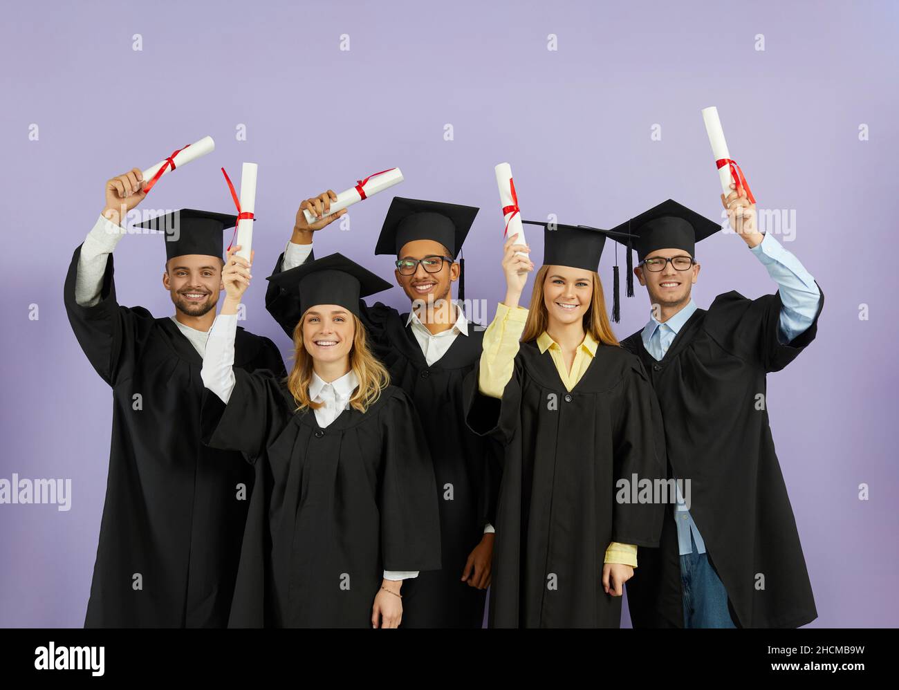 Felice università multirazziale laureati in berretti e camici che tengono in mano i diplomi e sorridenti Foto Stock