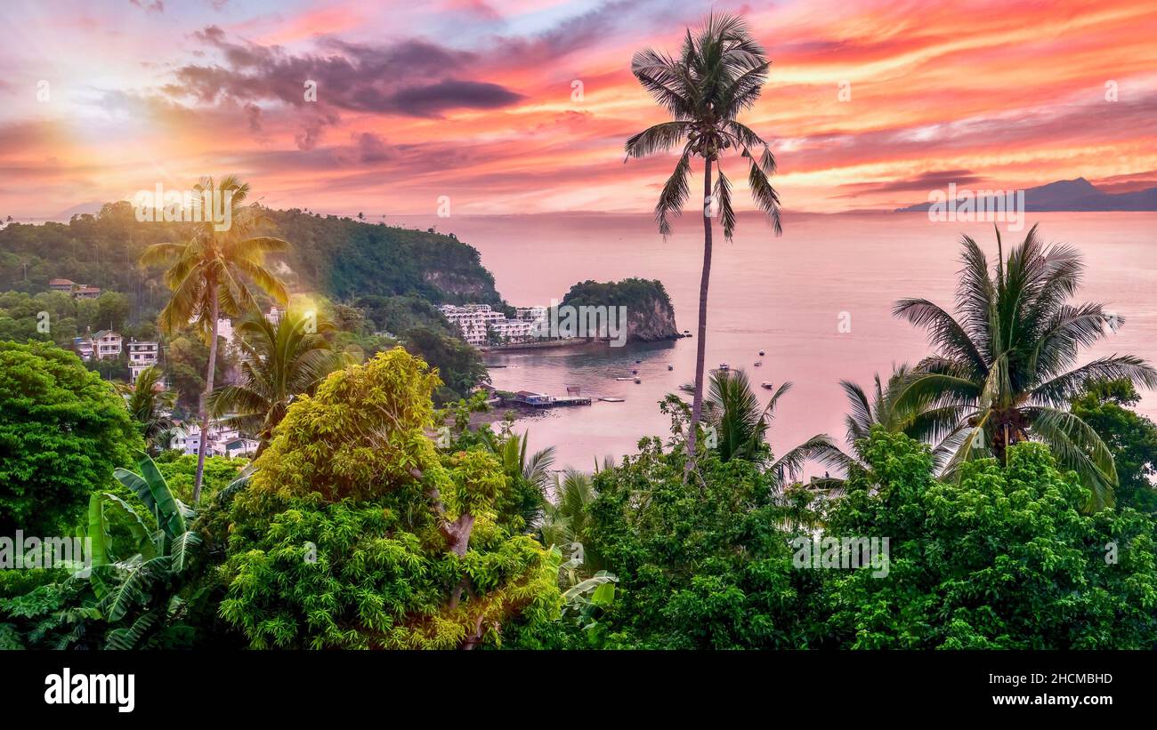 Vista ad alto angolo della popolare località di immersione di Sabang Beach a Puerto Galera, Oriental Mindoro, Filippine, con un bel cielo rosa tramonto. Foto Stock