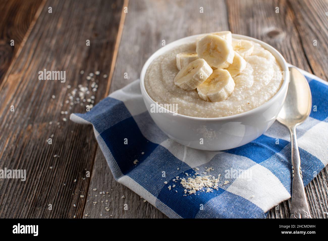 Recipiente per la colazione leggero con un porridge di miglio cucinato fresco servito con banani freschi isolati su tavola di legno con cucchiaio Foto Stock