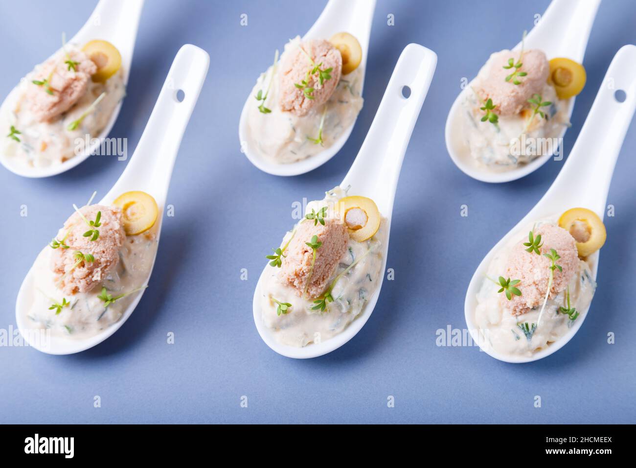 Antipasto freddo composto da fegato di merluzzo, caviale di merluzzo, olive, cetriolo e micrograni su cucchiai da servire. Piatto freddo tradizionale. Primo piano, piastra blu, nero Foto Stock