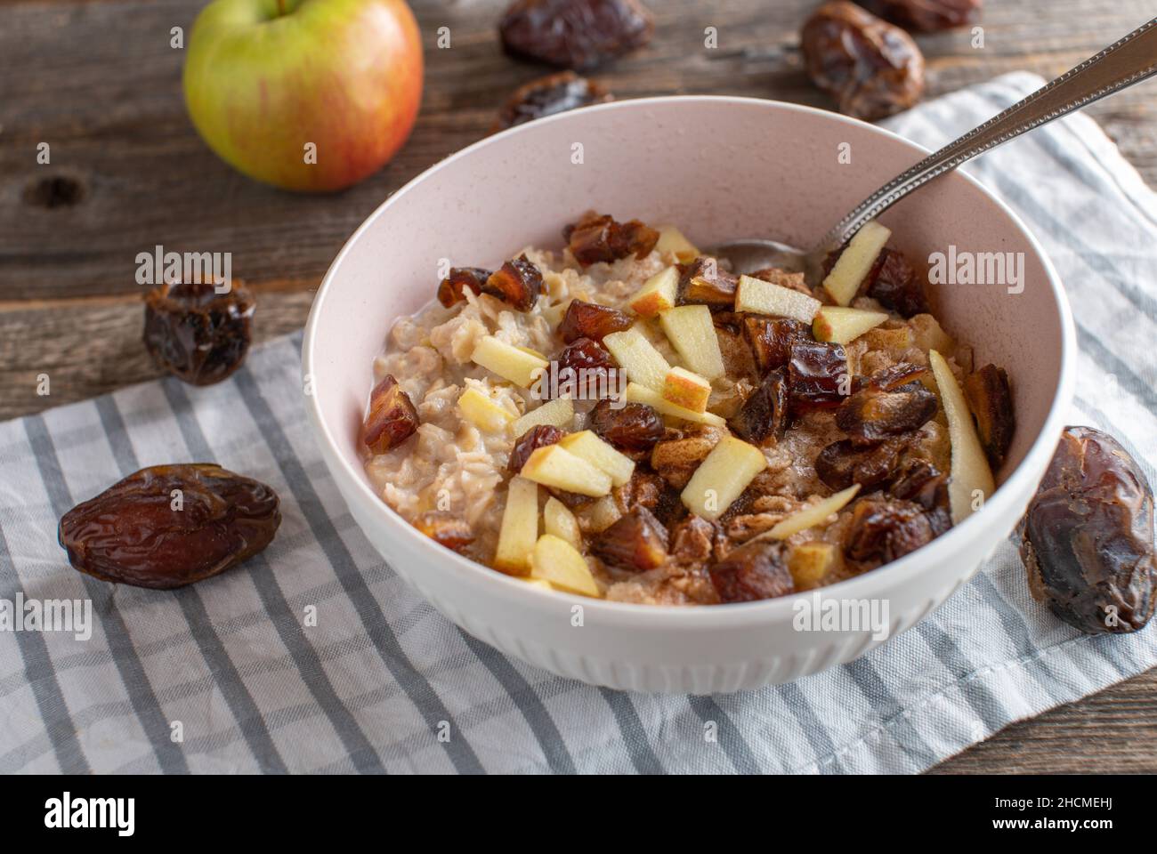 Porridge con mele e datteri di medjool servito in una ciotola con cucchiaio su sfondo rustico e tavola di legno Foto Stock