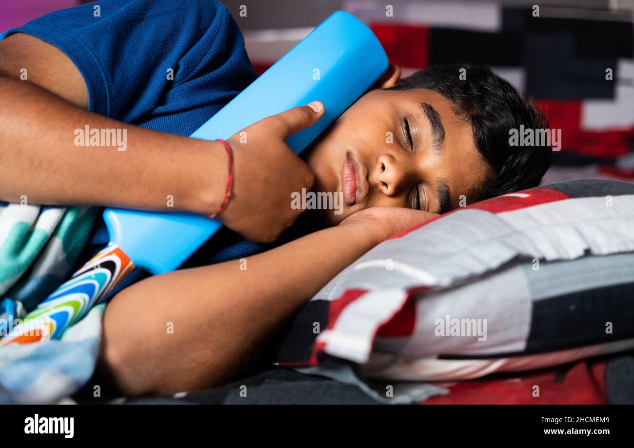 Bambino adolescente che dorme tenendo il pipistrello del cricket - concetto di sogno d'infanzia di diventare cricketer, giocatore e obiettivo. Foto Stock