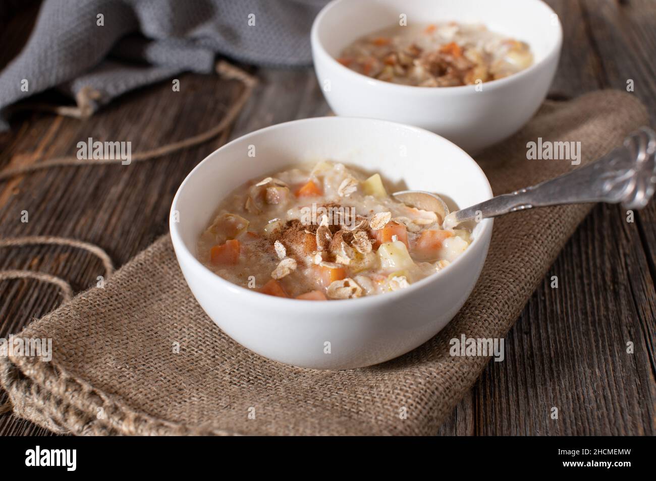 Porridge con mele cotte e patate dolci. Servito con cannella in una ciotola con cucchiaio su tavola di legno Foto Stock