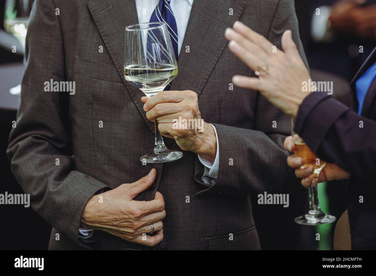 Dettagli con un uomo e una donna che interagiscono in un evento di classe, mentre tengono bicchieri di vino bianco. Foto Stock