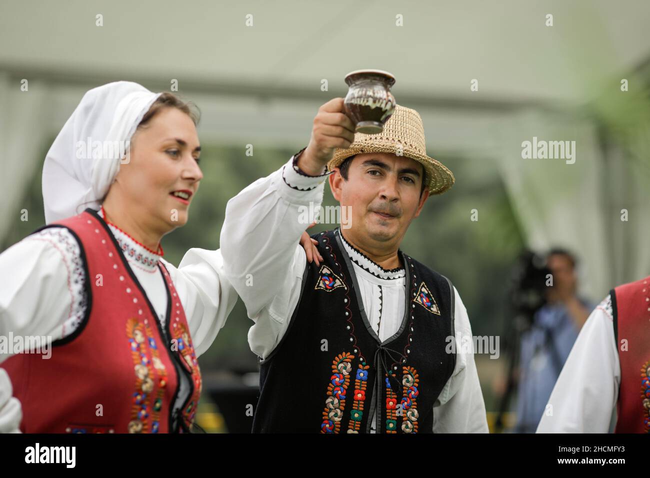 Braila, Romania - 26 agosto 2021: Uomini e donne vestiti con costumi tradizionali rumeni eseguono una danza tradizionale e bere tuica o palinca, un Ro Foto Stock