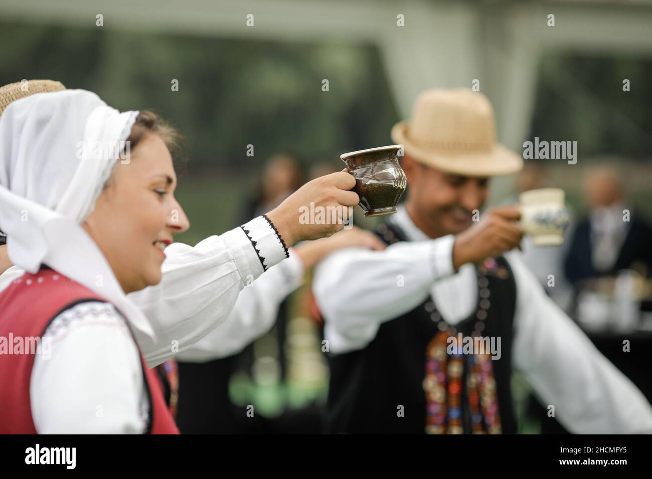 Braila, Romania - 26 agosto 2021: Uomini e donne vestiti con costumi tradizionali rumeni eseguono una danza tradizionale e bere tuica o palinca, un Ro Foto Stock