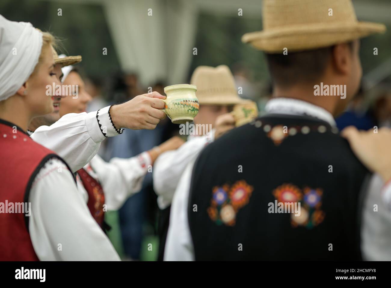 Braila, Romania - 26 agosto 2021: Uomini e donne vestiti con costumi tradizionali rumeni eseguono una danza tradizionale e bere tuica o palinca, un Ro Foto Stock