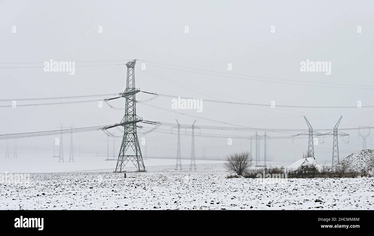 Piloni ad alta tensione in paesaggio invernale con neve. Il riscaldamento è costoso in inverno e i prezzi dell'elettricità in aumento in Europa. Foto Stock