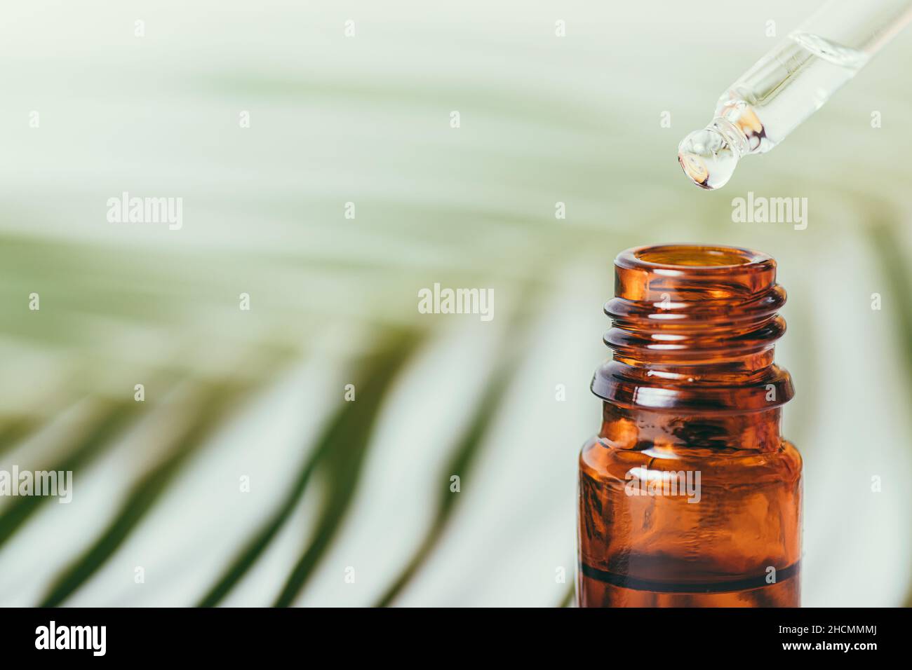 Gocciolamento di olio essenziale dalla pipetta in un flacone di vetro ambrato Foto Stock