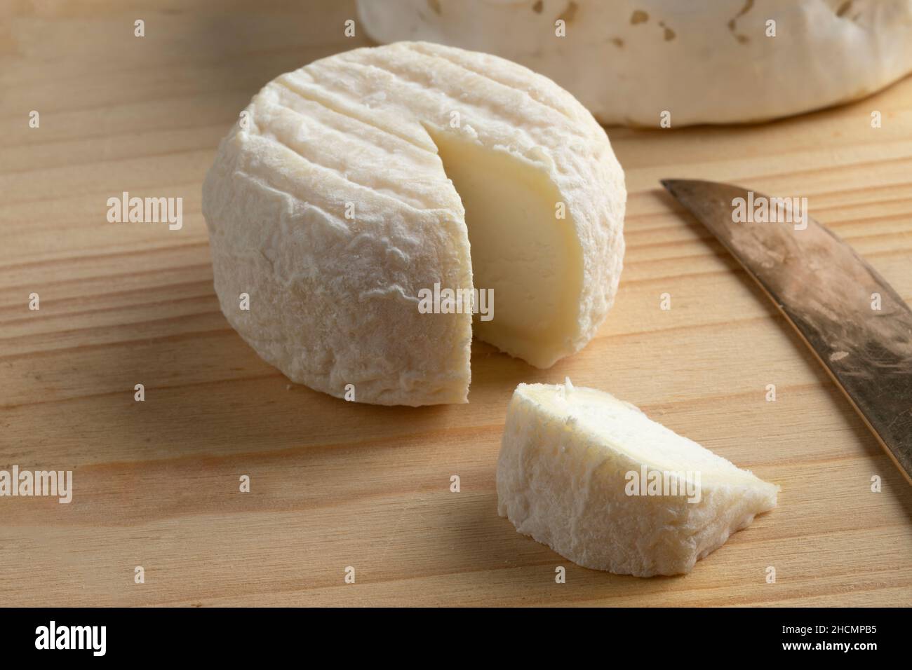 Singolo formaggio di capra francese, Crottin de Pays, e un pezzo da vicino su un tagliere di legno Foto Stock