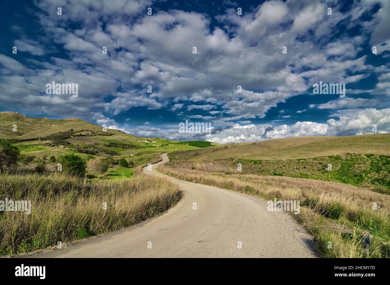 Tortuosa strada di campagna in una zona rurale della Sicilia nuvoloso e l'agricoltura collinare Foto Stock