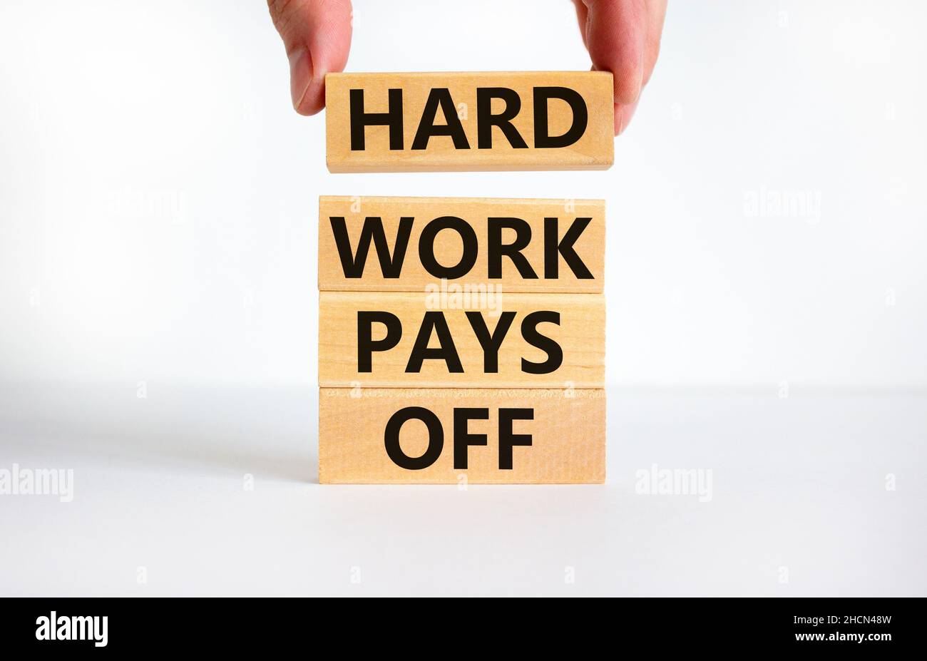 Il duro lavoro paga fuori simbolo. Parole di concetto il duro lavoro paga fuori sui blocchi. Mano dell'uomo d'affari. Bella tabella bianca, sfondo bianco, spazio per la copia. Affari Foto Stock