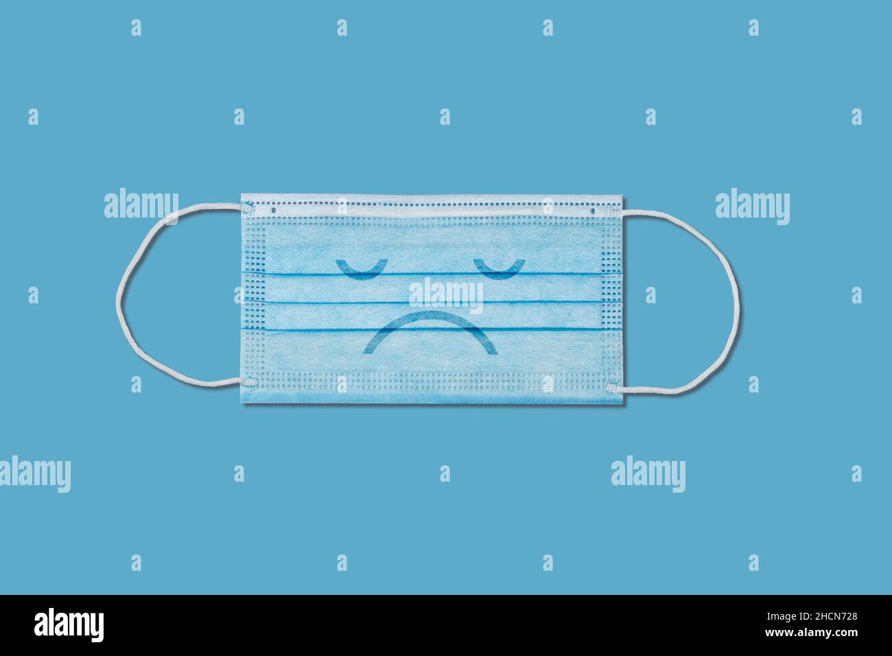 Maschera chirurgica con faccia triste su sfondo blu. Foto Stock