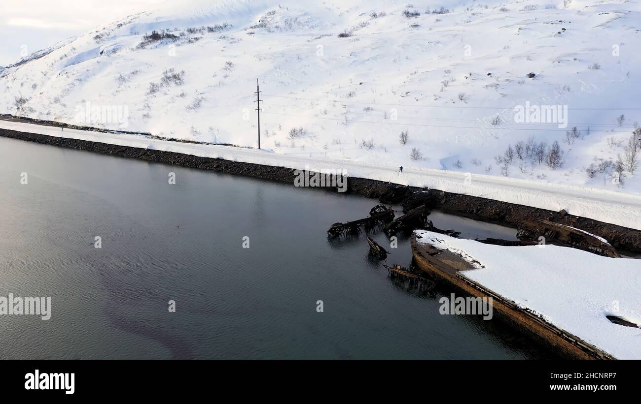Vista aerea della costa innevata invernale con barche in rovina dopo il naufragio. Vecchie barche da pesca affondate sulla riva del Mare di Barents. Foto Stock
