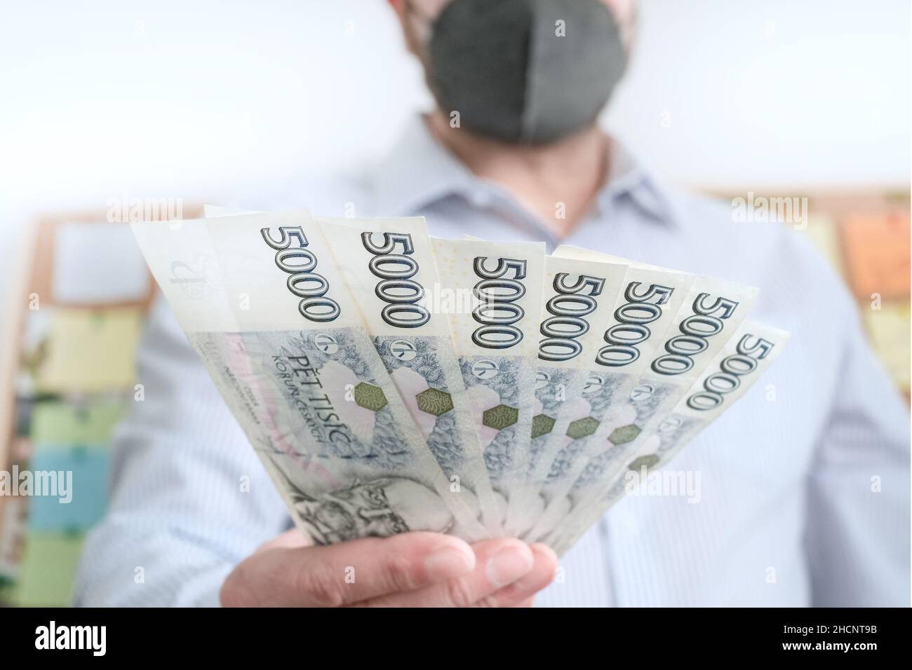 Finanza durante il coronavirus in Czechia Concept. Czech Koruna CZK 5000 banconote. L'uomo in un respiratore protettivo della maschera medica del viso tiene krona contanti. Foto Stock