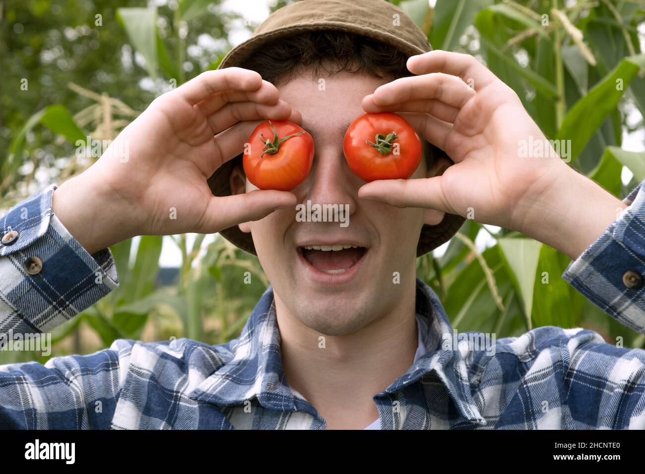 Ritratto positivo di Teenager fotolante intorno e sorridente, sta nascondendo il suo occhio dietro un pomodoro rosso. Teen che ha occhi divertenti coprenti con piccolo pomodoro-li Foto Stock