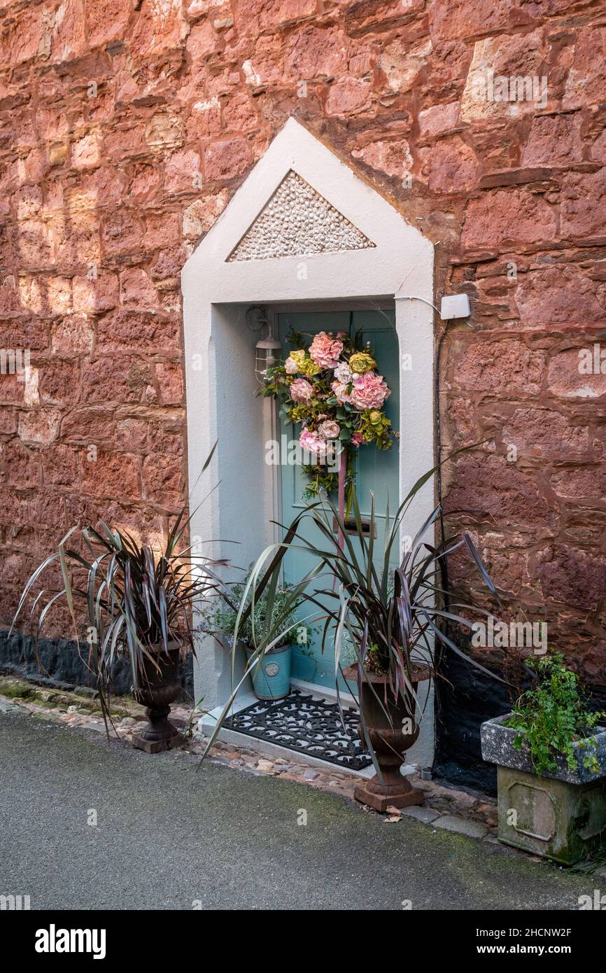 La porta d'ingresso inutilizzata di questa vecchia casa in pietra di Cawsand è stata decorata con una corona floreale e alcuni vasi ornamentali di piante. Cornwall, Regno Unito Foto Stock