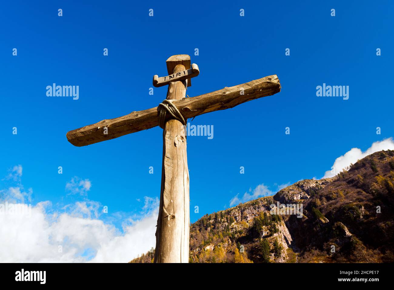 Antica croce di legno (tronchi di alberi) legata con corde con cielo blu e nuvole nel Parco Nazionale dell'Adamello Brenta. Trentino Alto Adige, Italia Foto Stock