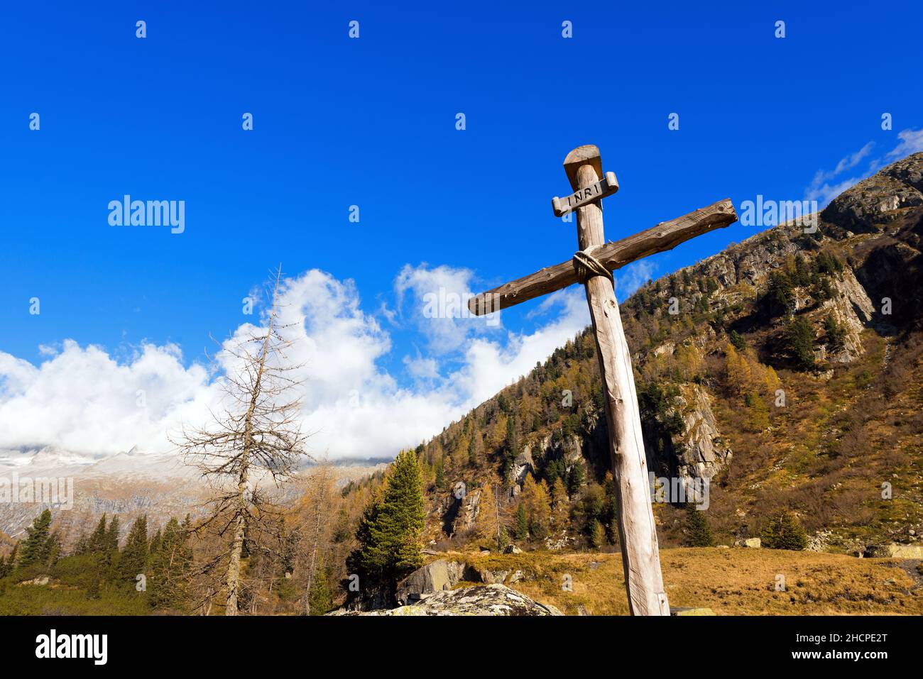 Antica croce di legno (tronchi di alberi) legata con corde con cielo blu e nuvole nel Parco Nazionale dell'Adamello Brenta. Trentino Alto Adige, Italia Foto Stock