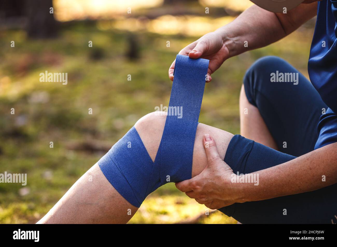 Pronto soccorso dopo incidente escursionistico. Ferito escursionista che mette elastico bendaggio al suo ginocchio. Problemi di tendine o ginocchio di pioggia durante il trekking in natura Foto Stock