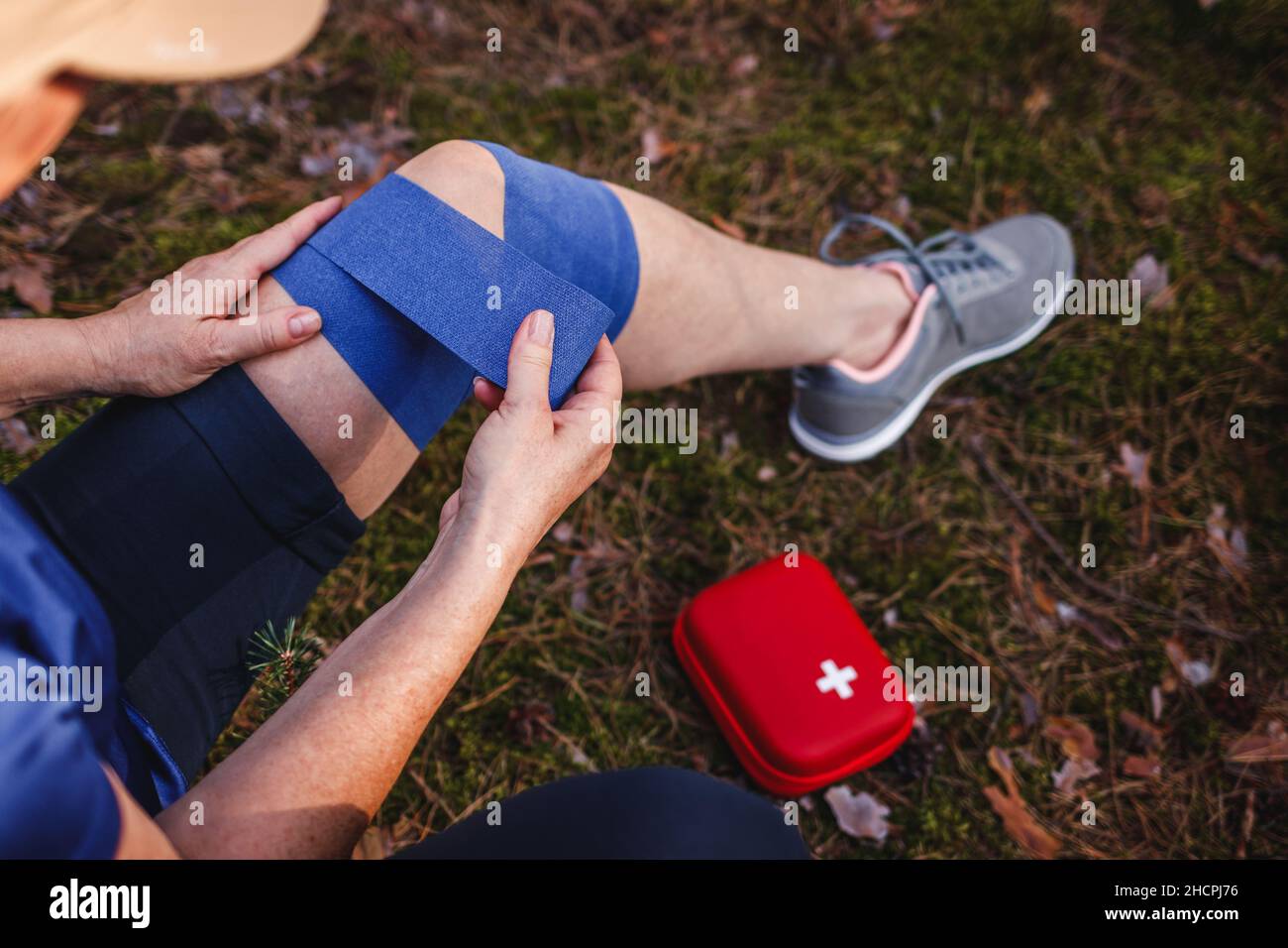 Fissazione della pioggia del ginocchio durante le escursioni. Donna ferita con fasciatura elastica del kit di pronto soccorso Foto Stock