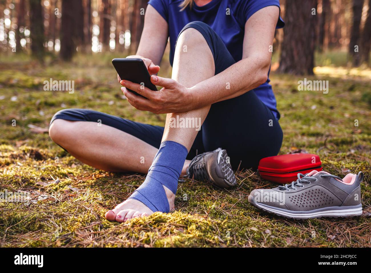 Un escursionista ferito con caviglia che utilizza lo smartphone per ottenere aiuto. La donna si è data il primo soccorso durante le ferite da trekking in natura Foto Stock