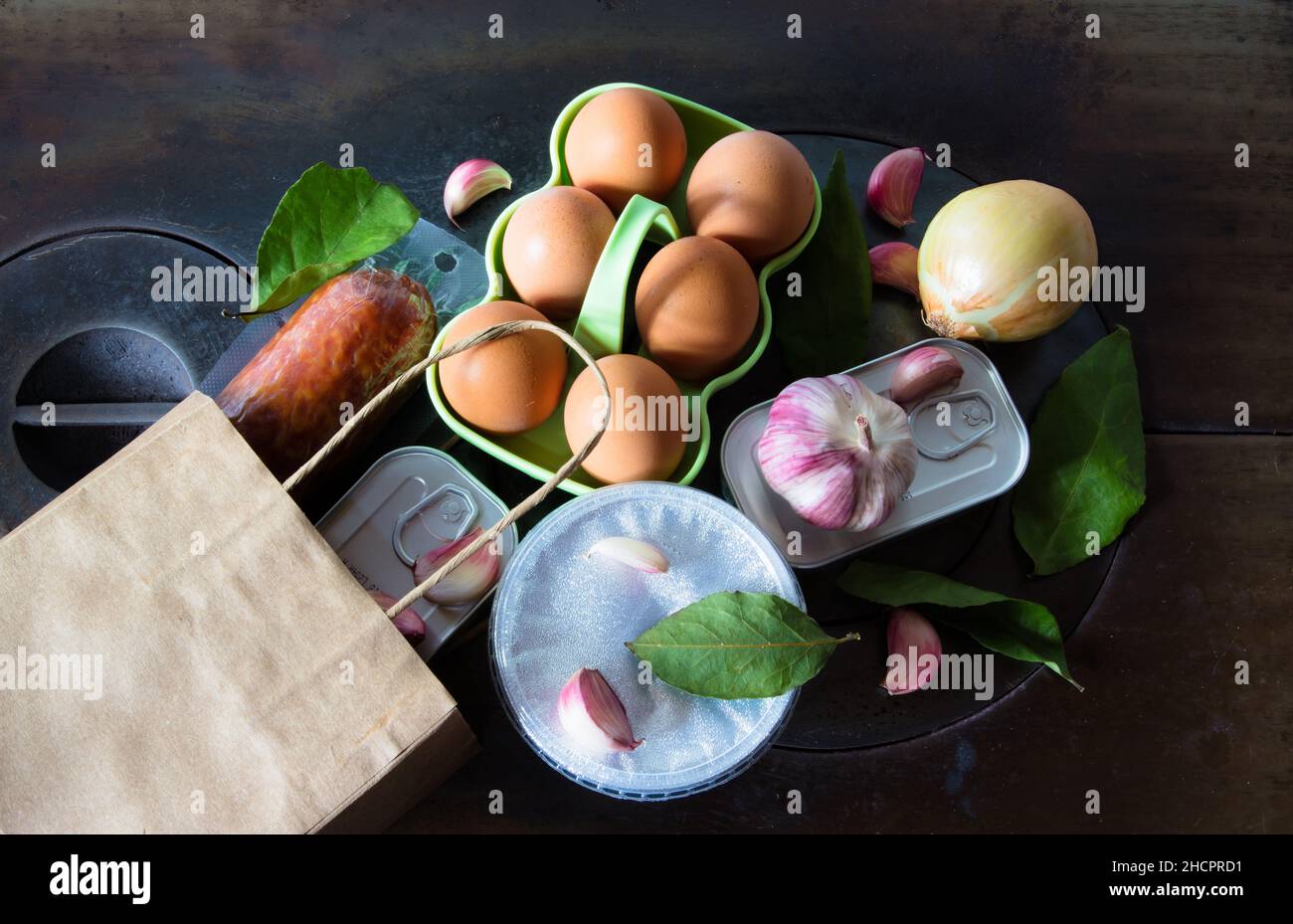 Sacco di carta riciclata con gli acquisti di cibo dal mercato sulla piastra di ferro della stufa a legna. Cibo scuro - cucina scura. Foto Stock