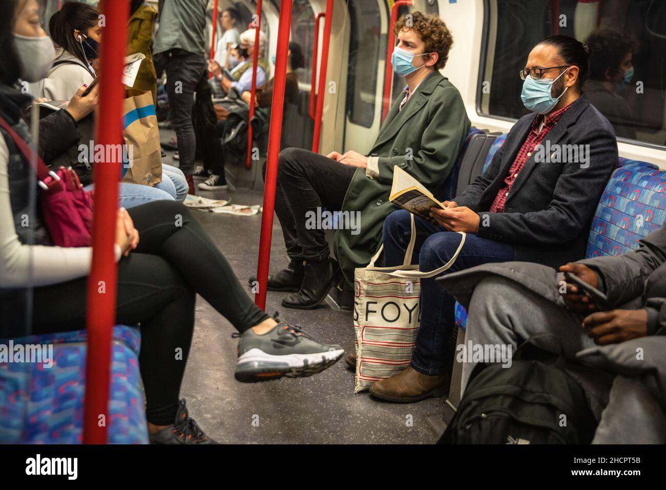 Persone che indossano maschere per il viso durante il Covid 19 pandemic, passeggeri su un treno metropolitana di Londra, Londra, Regno Unito Foto Stock