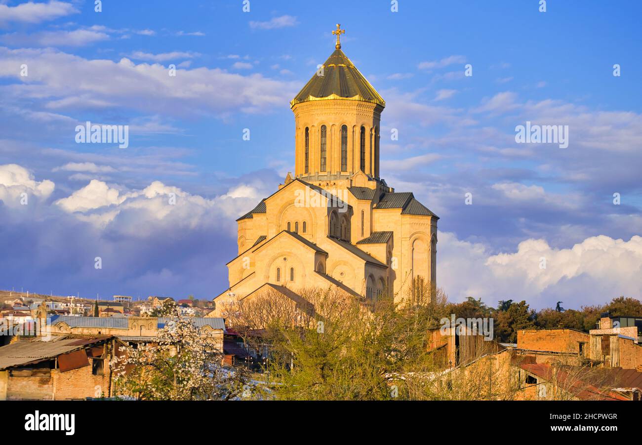 Chiesa della santa trinità Orthodox a Tbilisi con molti hosues intorno e alberi di primavera in fiore. Religione e cultura di Kartveliani. Sakartvelo. Foto Stock