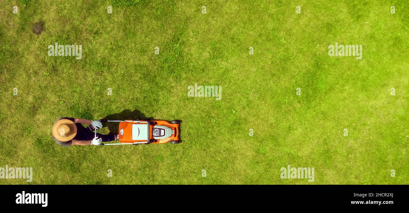 Un uomo sta falciando un prato con un rasaerba nel suo bellissimo giardino floreale verde Foto Stock