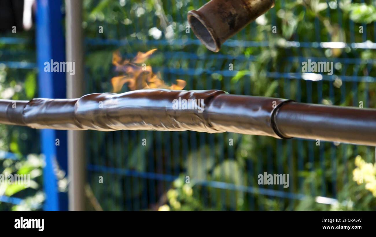 Guaina termorestringente per l'isolamento dei fili di fronte alla recinzione blu su sfondo verde di alberi. Processo di protezione dei fili, guaina termorestringente. Foto Stock