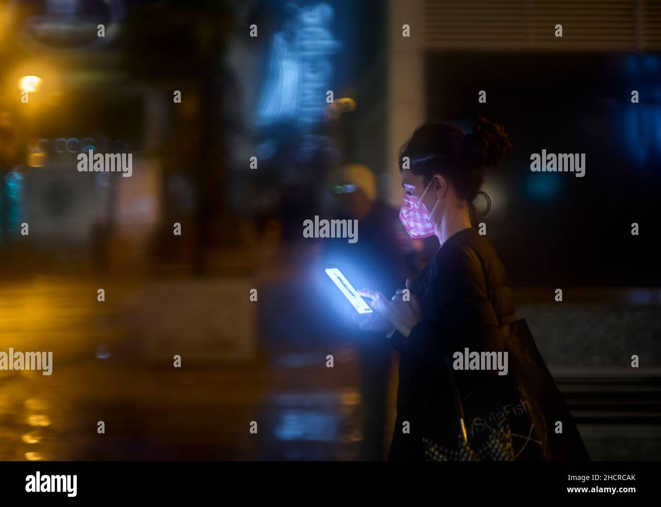 Una donna protetta da una maschera di consulenza il suo telefono cellulare. Foto Stock