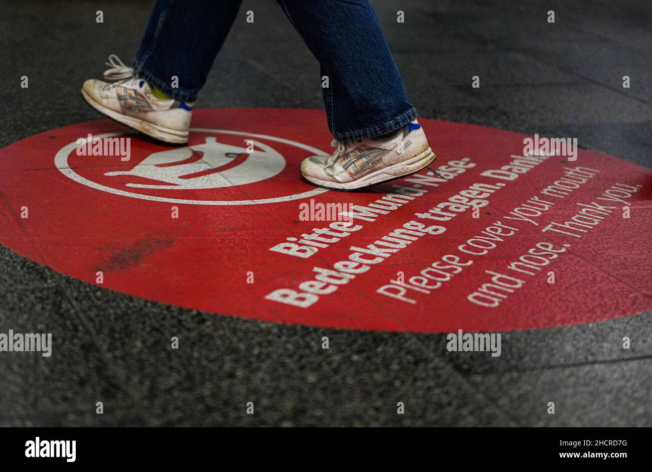 Grande cerchio circolare sul pavimento piattaforma della stazione Marienplatz di Monaco con una richiesta di coprire bocca e naso. È possibile vedere i piedi dei passeggeri. Foto Stock