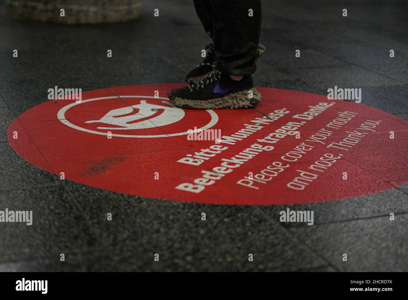 Grande cerchio circolare sul pavimento piattaforma della stazione Marienplatz di Monaco con una richiesta di coprire bocca e naso. È possibile vedere i piedi dei passeggeri. Foto Stock