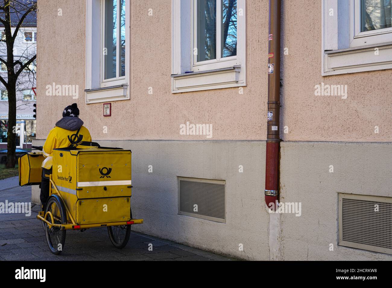 Un postino DHL fa una pausa. È seduto sulla sua bicicletta gialla con un rimorchio del contenitore che tiene la posta quotidiana per la sua zona. Foto Stock