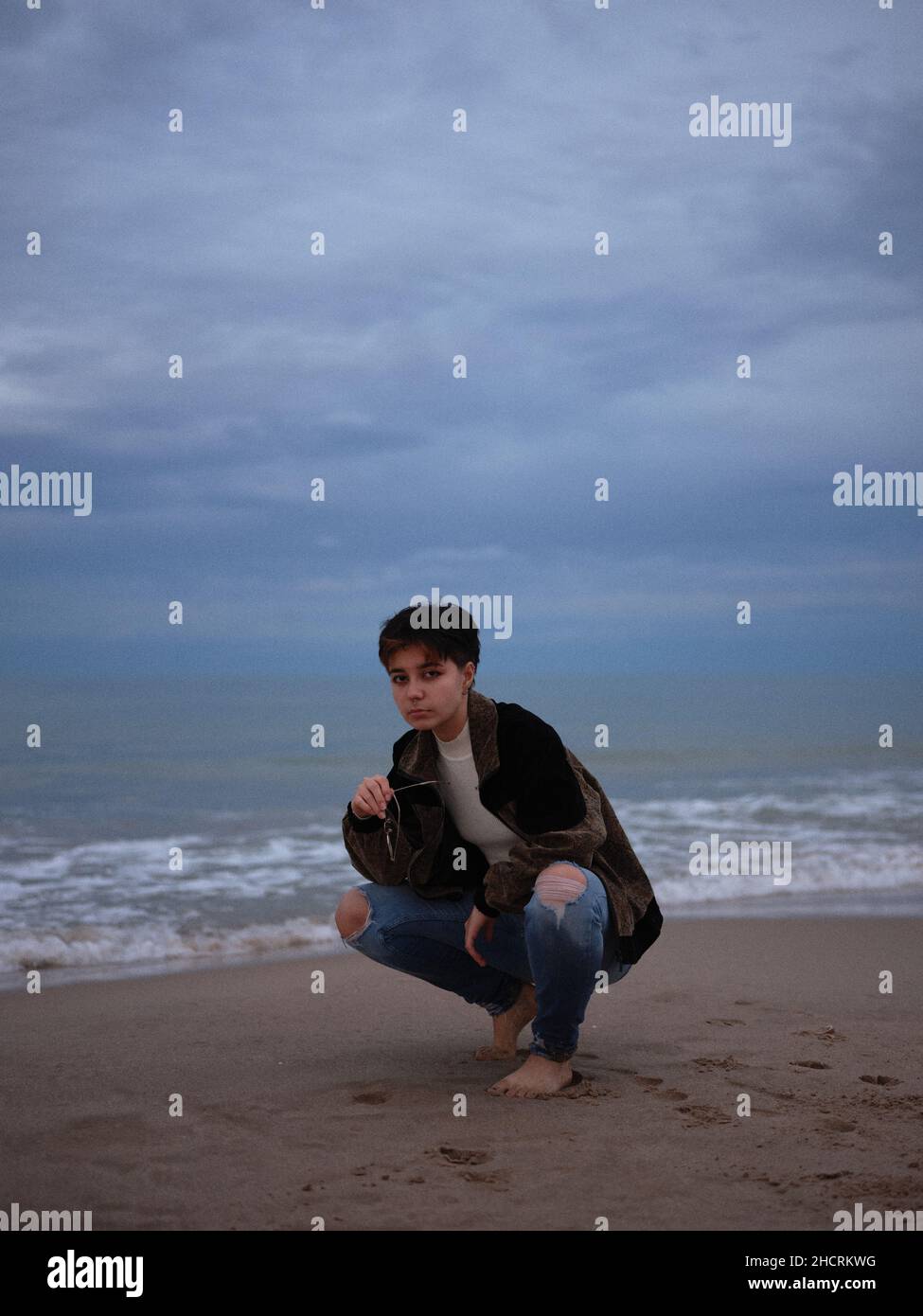 donna transgender che si piega guardando la fotocamera con gli occhiali in mano Foto Stock